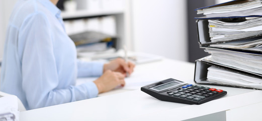 Calculator and binders with papers are waiting to be processed by business woman or bookkeeper back...
