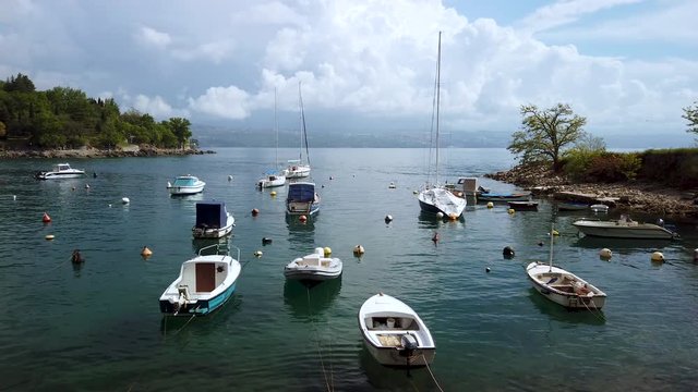 Panning shot across luxurious old landscape panorama. Lovran, Croatia harbour, boats moored along the waterfront. Holiday seascape. Various colourful boats floating on reflecting waters.