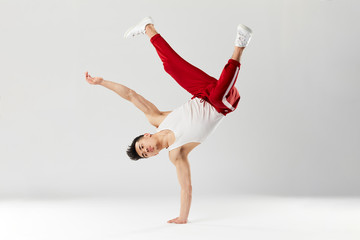 Athletic young b-boy standing on one hand while dancing break dance and doing downrock isolated over white studio background.