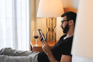 Relaxed man reading an ebook or tablet laying on a comfortable bed