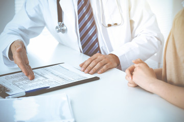 Doctor and patient woman discussing something at the desk in hospital office. Concepts of medical ethics and helping people in medicine