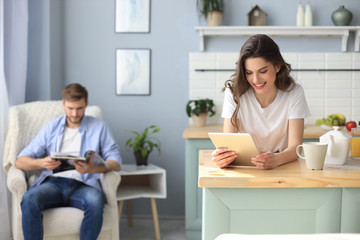 Smiling beautiful woman using laptop with blurred man in background at home.
