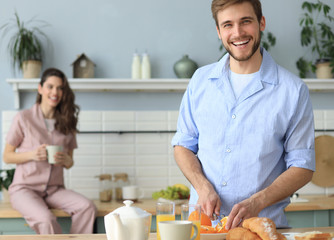 Portrait of happy young couple in pajamas cooking together in the kitchen, drinking orange juice in the morning at home.