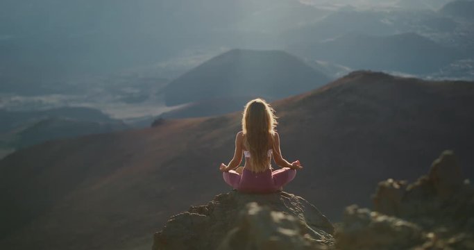 Young peaceful woman meditating on the top of a mountain, zen yoga meditation practice in nature