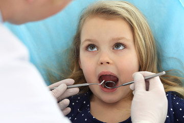 Little baby girl sitting at dental chair with open mouth and feeling fear during oral check up while doctor. Visiting dentist office. Medicine concept