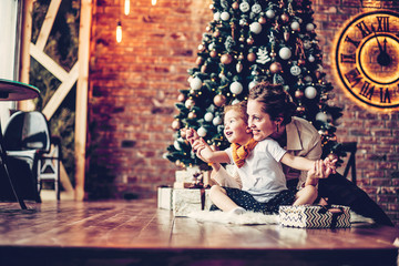 Obraz na płótnie Canvas mom plays with her daughter, sitting near the Christmas tree