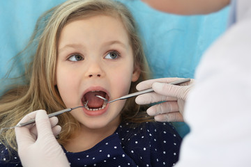 Little baby girl sitting at dental chair with open mouth and feeling fear during oral check up while doctor. Visiting dentist office. Medicine concept