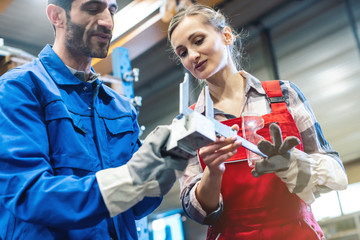 Woman and man worker checking measurements of metal work piece