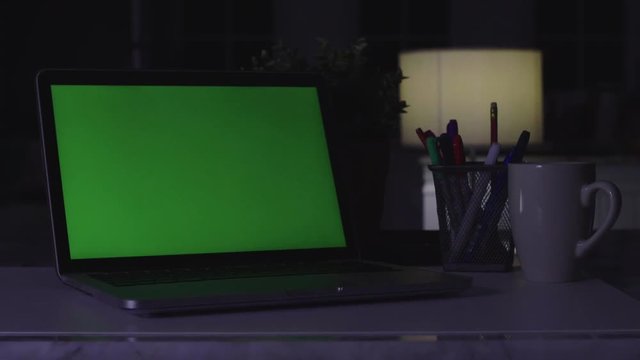 Laptop with green screen. Dark office. Dolly shot. Perfect to put your own image or video.