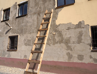 An old building with damaged facade with wooden ladder by the wall