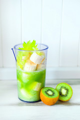 Green smoothie of celery and banana. Cut halfs of kiwi on table. Healthy vegan lifestyle