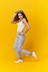 Style, fashion, beauty and summertime concept. Studio shot of cheerful attractive cute girl wearing light cotton top and striped trousers posing at yellow wall, being in good mood. Vertical image