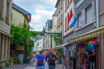 Narrow street in old town of Echternach, in Luxembourg, Europe. Typical houses with flags and tourists walking - obrazy, fototapety, plakaty