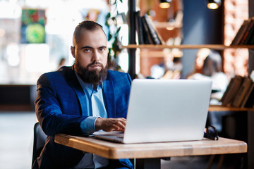 Businessman bearded man in a suit works behind the laptop sitting in a comfortable office coworking.