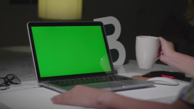 Laptop with green screen. Dark office. Dolly shot. Perfect to put your own image or video.