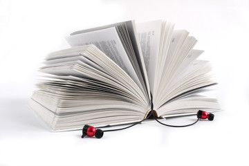 Concept to listen to audio books. White headphones on the open book. White background with space for text