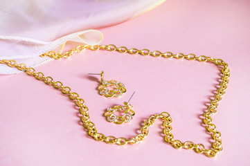 Luxury gold jewelry chain and earrings on pink background with silk, copy space, selective focus