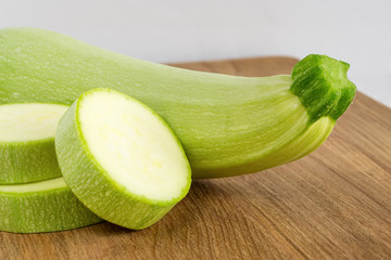 Close-up of fresh green zucchini and few slices on a brown wooden cutting board. Cook at home. Fresh farm vegetables and healthy vegetarian food.