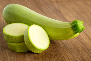 Two fresh green zucchini and few slices on a brown wooden cutting board. Cook at home. Fresh farm vegetables and healthy vegetarian food.