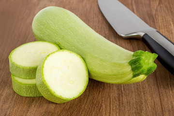 Fresh green courgettes, few slices and chef knife on a brown wooden cutting board. Cook at home. Fresh farm vegetables and healthy vegetarian food.