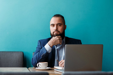 Businessman bearded man in a suit works behind the laptop sitting in a comfortable office coworking.