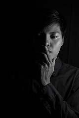 Studio portrait of a Thai Asian LGBT,women handsome beautiful young man  standing on black backdrop is blue shirt with feeling,think on face. black and white photo