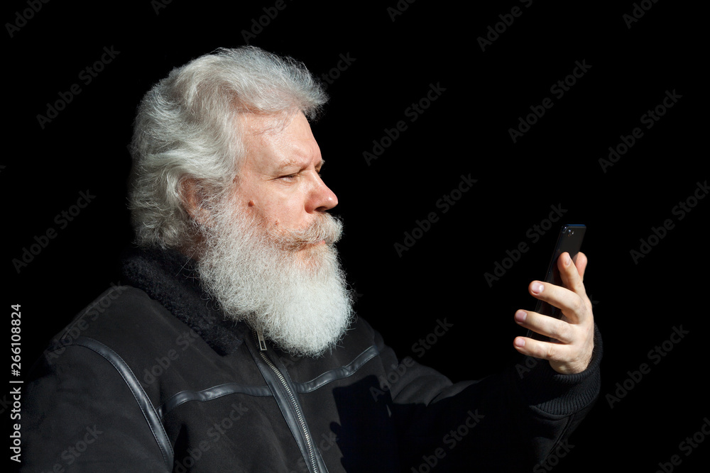 Wall mural handsome senior man looking at smartphone against black background. close up profile portrait of eld