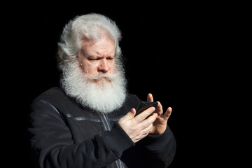 Handsome senior man using smartphone against black background. Close up face portrait of elderly stylish male with splendid mustache and beard wearing dark flight (bomber) jacket.