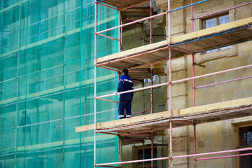 restoration of the Gatchina Palace. worker stands on scaffolding. part of the palace is covered...