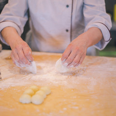 Close-up of female hands in white cook coat knead the dough on the wooden table in the restaurant