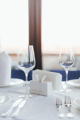 Close-up table in a restaurant. Glasses for wine, forks, spoons, napkins on a blurred light background