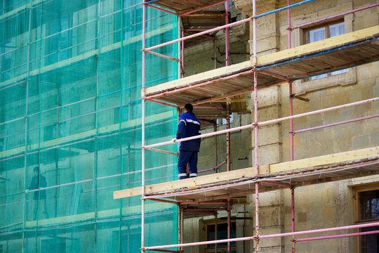 restoration of the Gatchina Palace. worker stands on scaffolding. part of the palace is covered with a protective green grid. reportage.