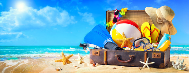 Beach accessories in suitcase on sand. Family holidays concept