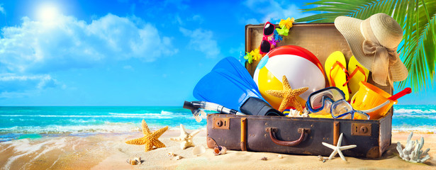 Beach accessories in suitcase on sand. Family holidays concept