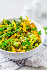 Green salad with spinach, pepper, cucumber, pesto sauce and sprouts in white bowl.