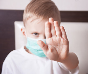 Little boy in face mask showing stop sign with her hand