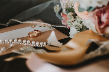 Two gold wedding rings with gemstones are among the accessories: bridal bouquet, cards, veils and lace ribbons. Photos in stylish dark colors, copy space, selective focus.