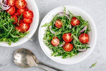 Healthy Green Fresh Arugula Salad Bowl with Tomatoes and Red Onions. Top view