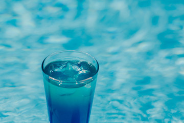 Blue coctail with ice in the glass on the swimming pool background. Resort tropical hotel in summer day and fresh water. Blurred backgraund with copy space.