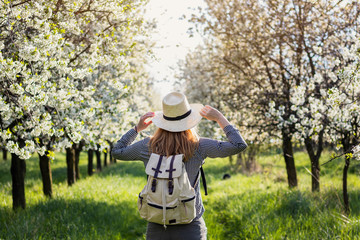Woman backpacker enjoying sunlight in blooming cherry orchard