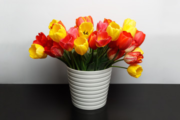 Large bouquet of yellow and red tulips in a large white vase is on the table