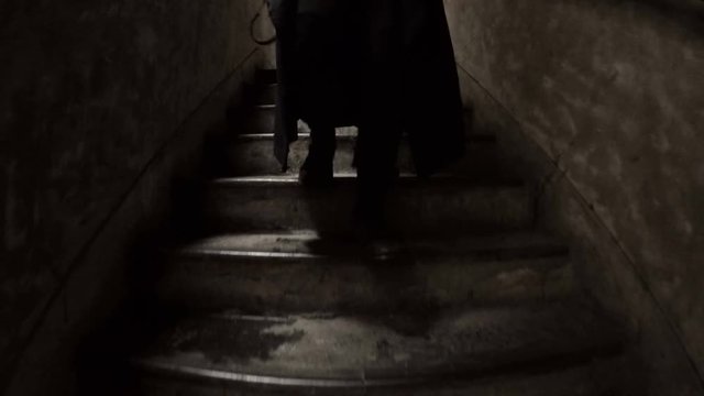 Mysterious feet walking down concrete steps. A stranger in boots descends a dark shadowy, dirty set of stairs in an industrial type of area. Stalker or killer following his victim.