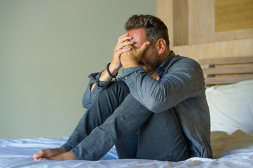 young attractive overwhelmed and depressed man sitting on bed worried and frustrated suffering depression crisis covering face with hands feeling desperate