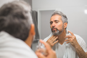 middle aged bearded gray haired man applying perfume in bathroom