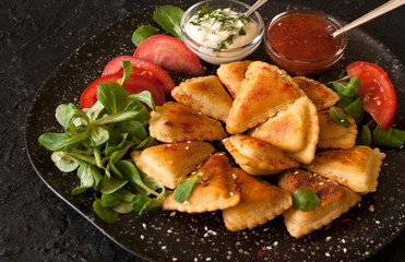 Small puff fried pies with vegetarian and meat fillings are served with sauces on a black slate Board.