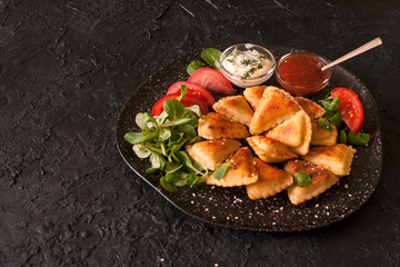 Small puff fried pies with vegetarian and meat fillings are served with sauces on a black slate Board. Copy space