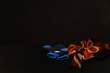Baby pink and blue socks with a bow are lying on a black table, on a black background.
