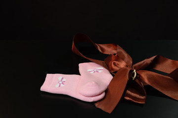 Baby pink socks with a bow are lying on a black table, on a black background.