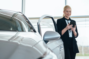 young blonde saleswoman in car showroom using tablet