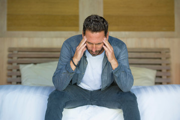 portrait of young attractive overwhelmed and depressed man sitting on bed worried and frustrated suffering depression crisis fired from work or divorce problem